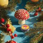 Decorative mushroom with a label on a blue surface surrounded by Christmas tree branches and ornaments.