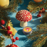 Decorative mushroom with a label on a blue surface surrounded by Christmas tree branches and ornaments.