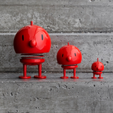 Three glossy red bird-shaped spring toys in different sizes standing on a concrete surface against a textured gray wall.