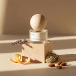 Perfume bottle with wooden cap on a wooden block, surrounded by dried lavender and nuts on a beige background.