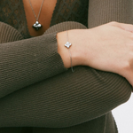 Person wearing a silver bracelet with a clover charm on a plain background