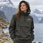 A woman wearing an olive green hooded Anorak jacket from The North Face stands outdoors in front of a dramatic mountain and fjord landscape.