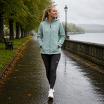 Woman walking on a rainy path wearing a light green jacket and black leggings.