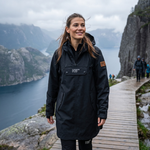 Woman in a black rain poncho standing on a wooden path with a scenic mountain and lake view.